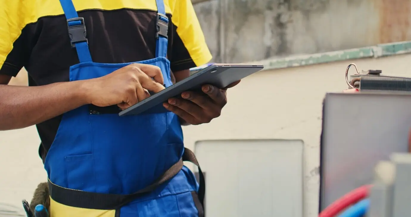 Close-up of a skilled technician assigned to routine maintenance on an outdoor HVAC system, checking for refrigerant issues. A meticulous mechanic inspecting the air conditioner, recording data on a tablet.